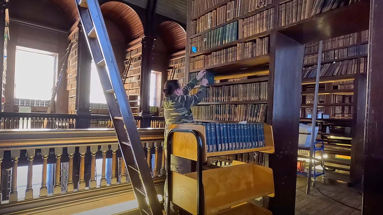 person replacing books on a shelf in an old library
