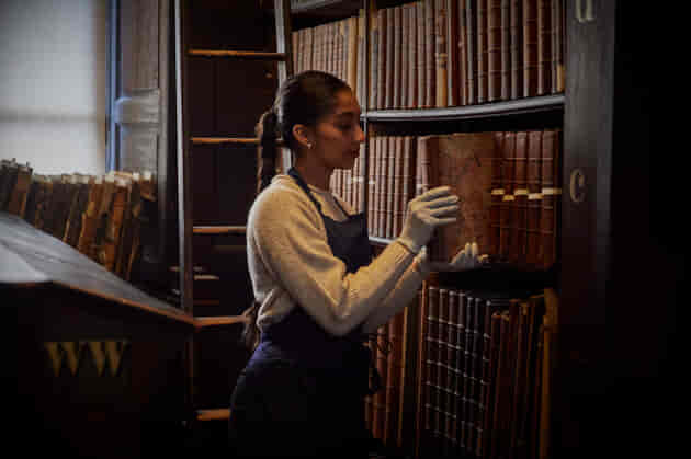 A library assistant removes a book from a shelf in the Long Room