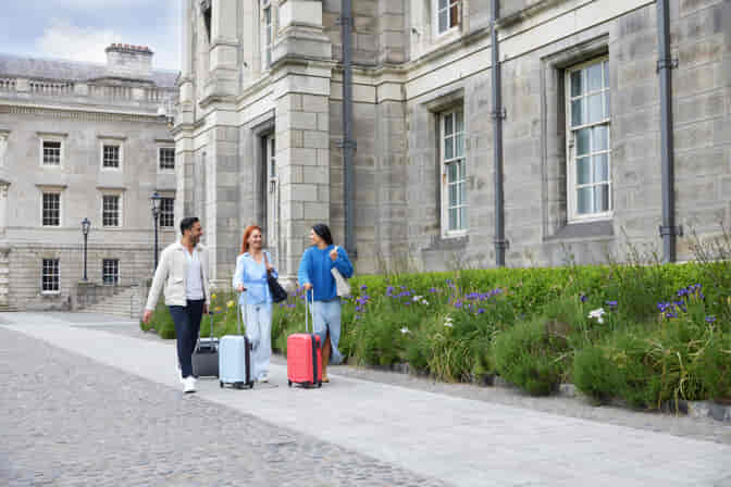 3 people walking with suitcases in Trinity's the Front Square cobbled pathways